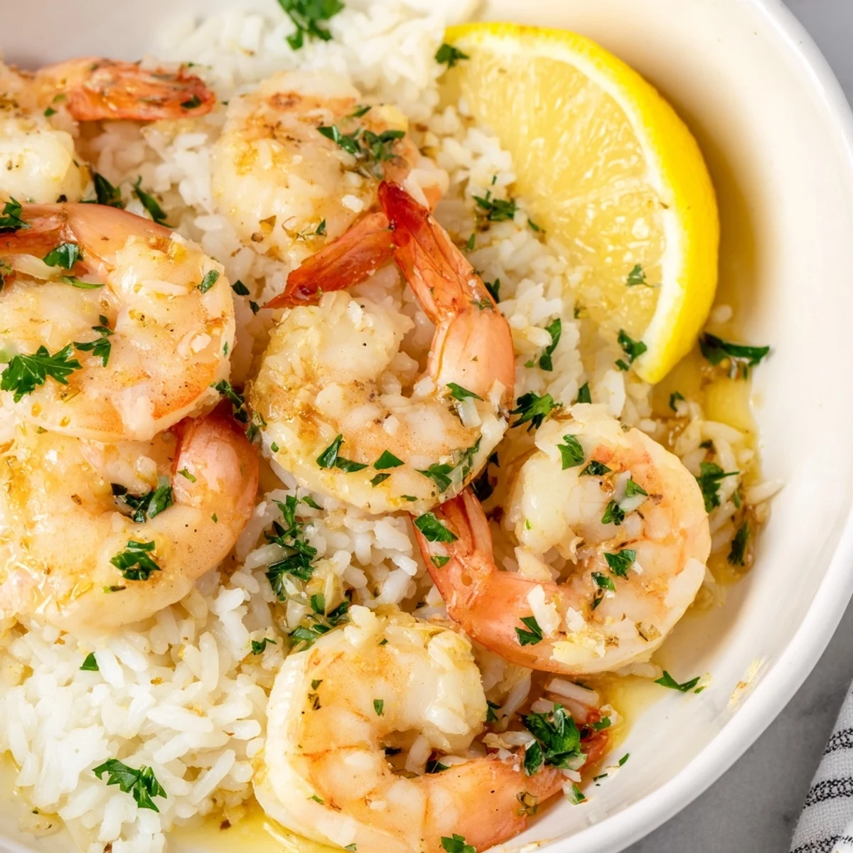 Close-up of garlic butter shrimp atop rice, featuring a vibrant lemon garnish for flavor and color.