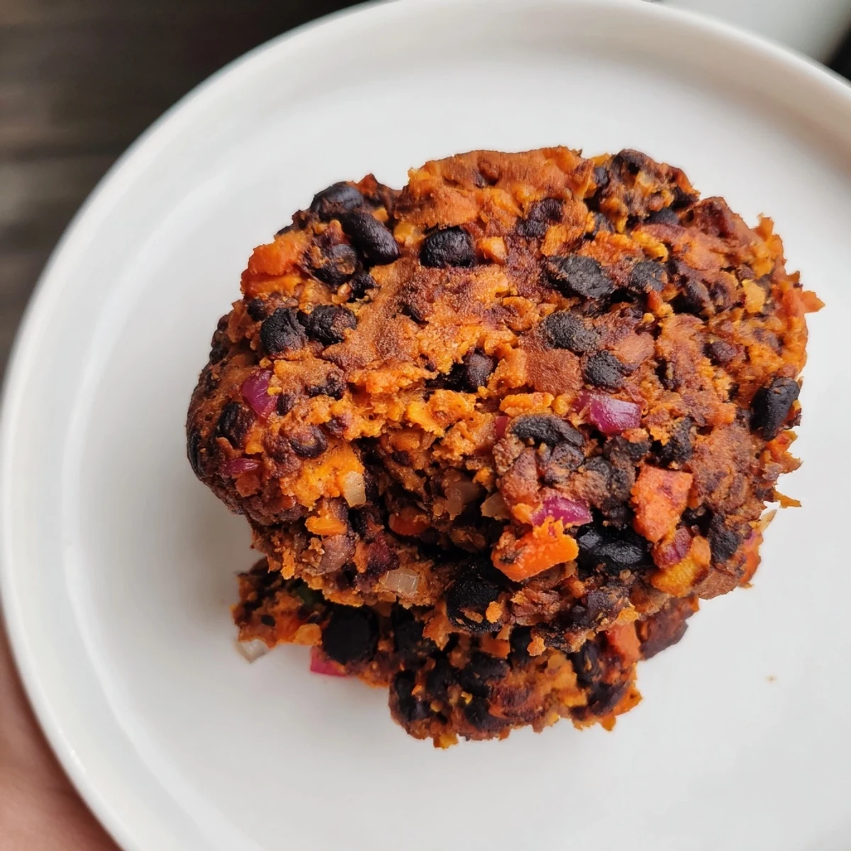 Golden-brown, crispy black bean burgers served on a toasted bun with fresh tomato slices and avocado.