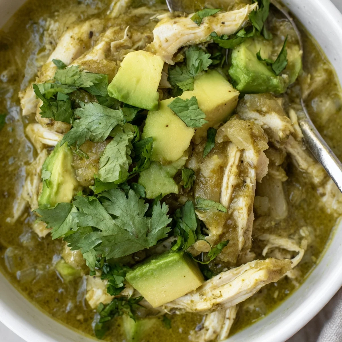 A hearty bowl of Chicken Chili Verde garnished with sliced radishes and lime wedges, served alongside warm corn tortillas for dipping.  