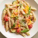 A close-up of One-Pot Creamy Pasta Primavera reveals a rich, creamy sauce coating the penne pasta.
