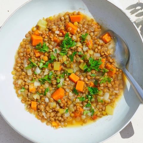 Steaming bowl of Lentil Soup with carrots and celery, garnished with fresh herbs, ready to serve.