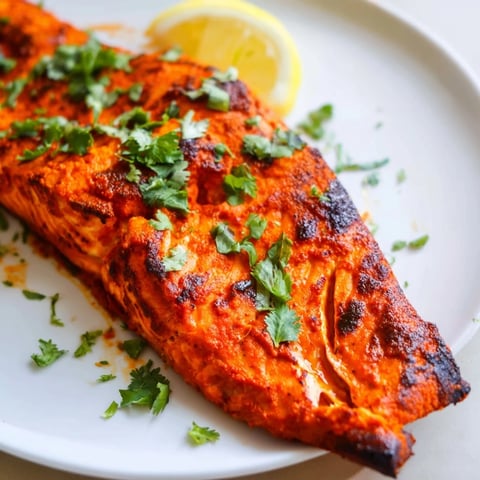 Vibrant Indian Tikka Salmon, beautifully roasted, served with fresh cilantro and a lemon wedge.