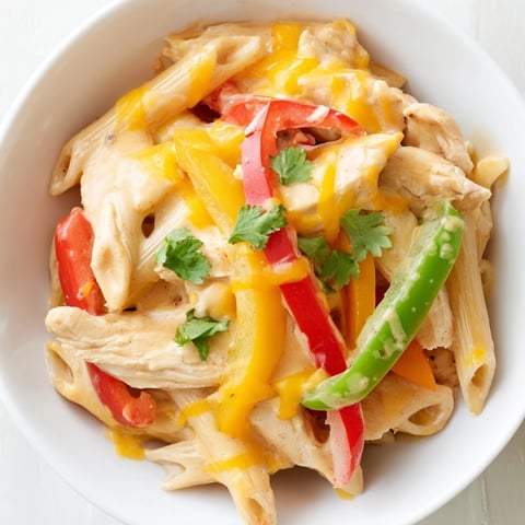 A steaming skillet of Chicken Fajita Pasta, topped with melted cheese, cilantro, and lime wedges on a rustic table.  