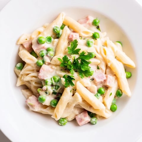 A steaming plate of Spring Pea & Ham Pasta features penne coated in a creamy sauce with vibrant green peas and diced ham.  