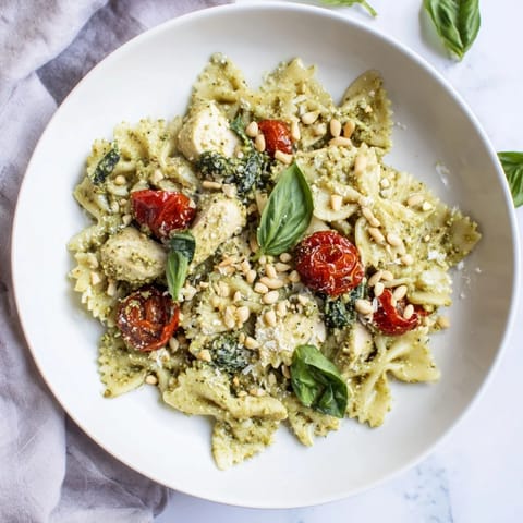 Vibrant pesto chicken bowtie pasta, garnished with cherry tomatoes and fresh basil leaves.