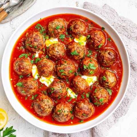 A close-up view of steaming Instant Pot Greek Meatballs, garnished with fresh herbs and feta.