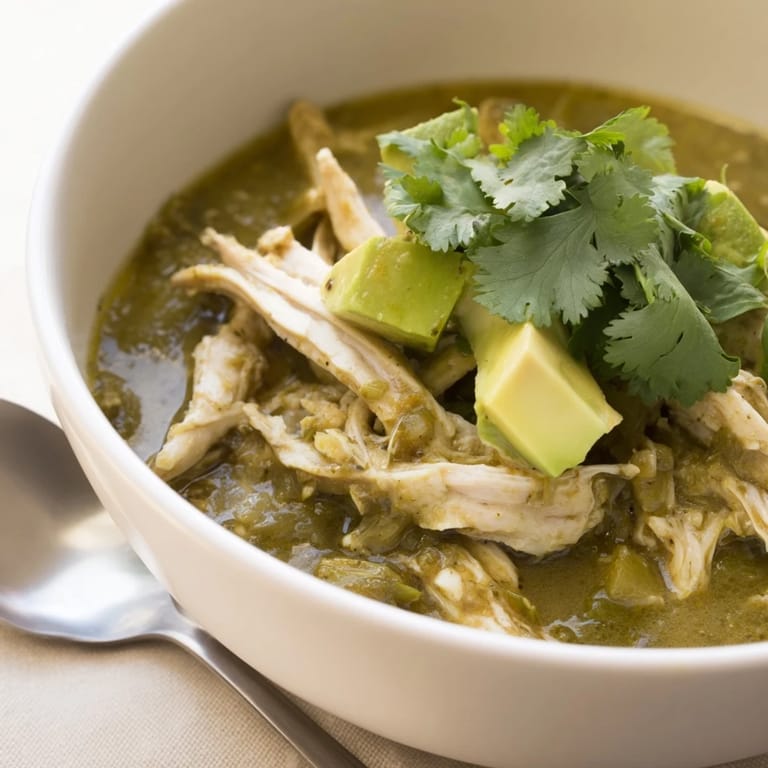 A rustic Dutch oven filled with Chicken Chili Verde, showcasing the rich, charred green sauce and tender chicken, ready for a comforting meal.
