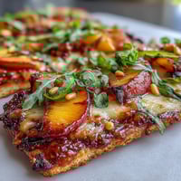 Grilled flatbread with peaches and Brie cheese, drizzled with BBQ sauce and fresh herbs.  